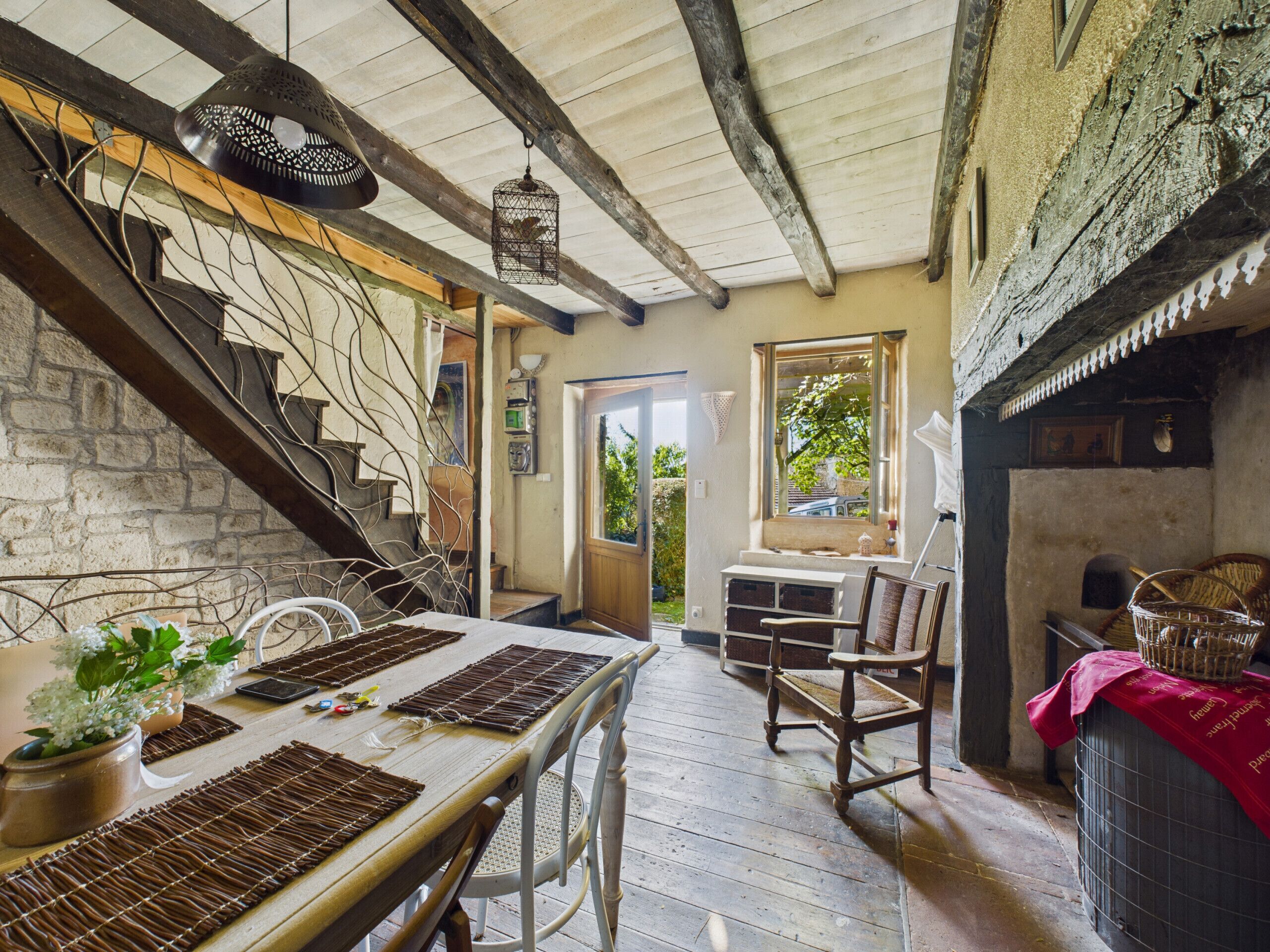 Un intérieur rustique avec un escalier en bois, une table à manger agrémentée de sets de table et une vue sur l’extérieur.