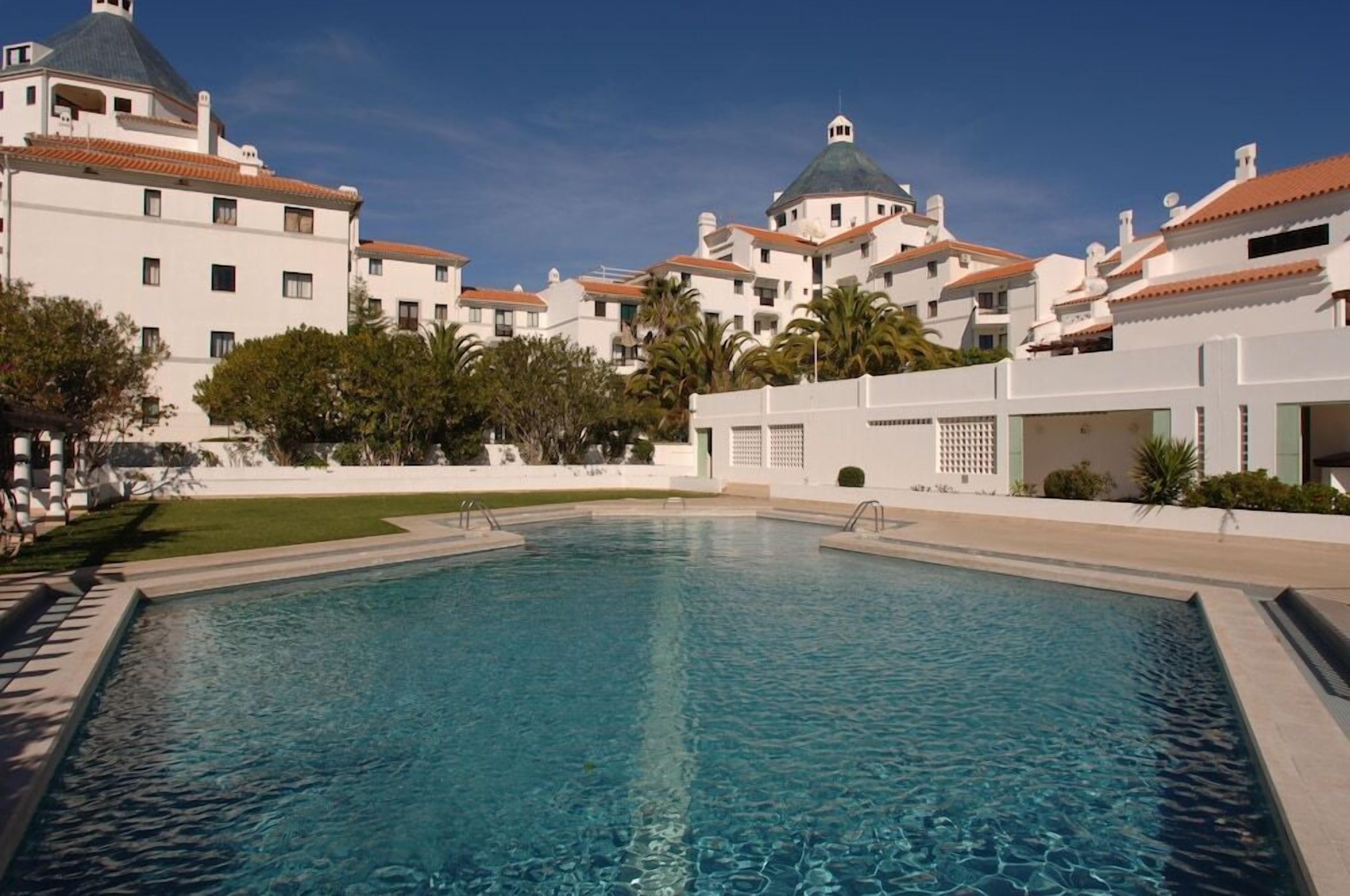 A swimming pool surrounded by buildings with white facades and red-tiled roofs.