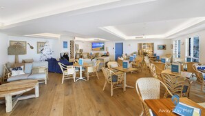 A spacious room with a large wooden dining table, wicker chairs, and a cozy seating area with a sofa and cushions. - Diggers Beach Studio - In Aanuka Beach Resort. Pools, Spa, Tennis, Restaurant (Coffs Harbour)