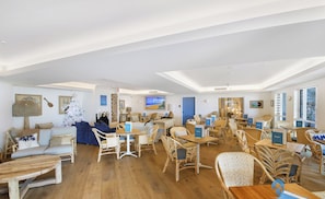 Um quarto espaçoso com uma grande mesa de jantar de madeira, cadeiras de vime e uma área de estar aconchegante com um sofá e almofadas.