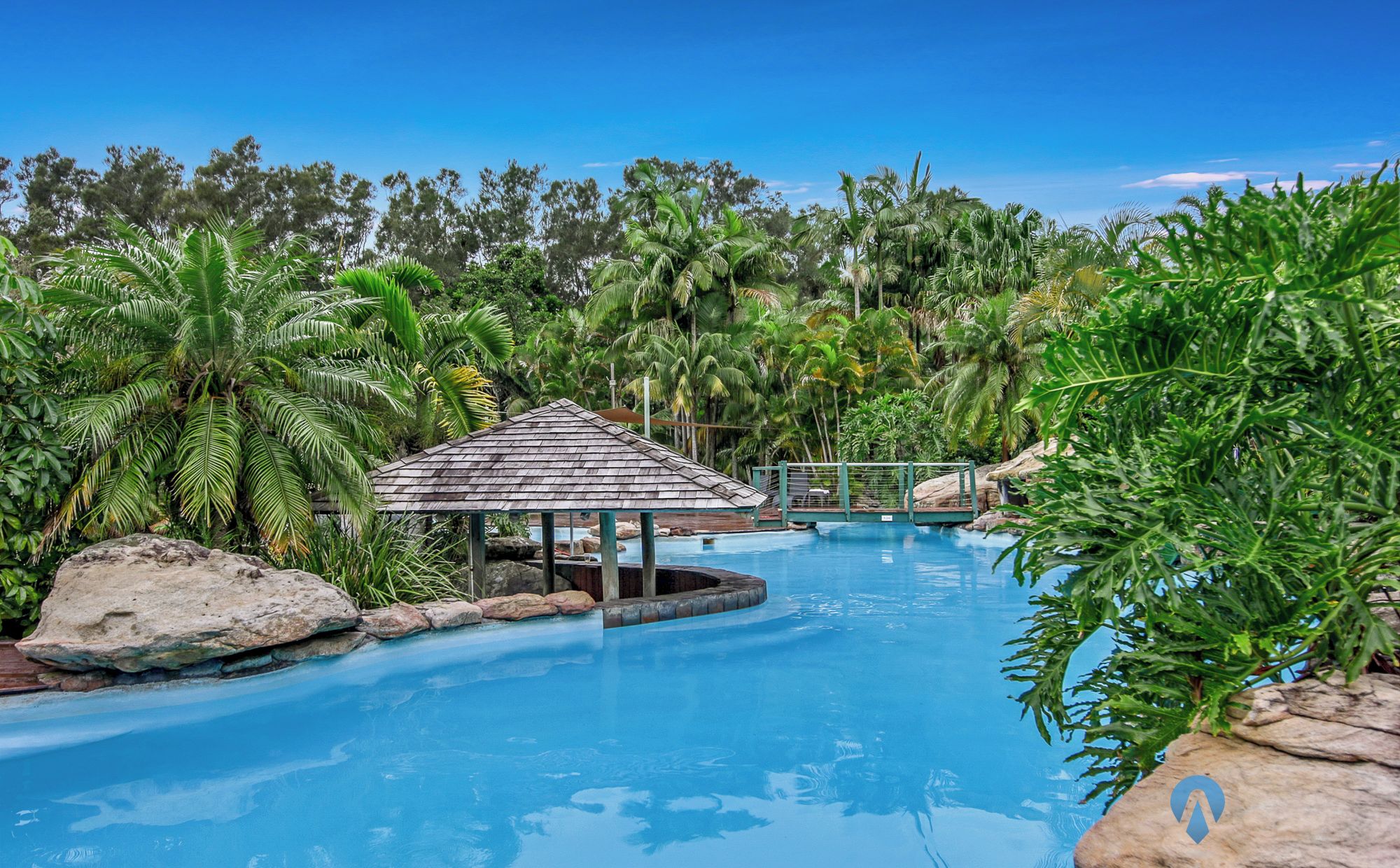 Area piscina con gazebo, circondata da vegetazione tropicale e rocce.