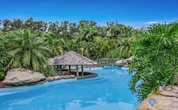Uma área de piscina com um gazebo, cercada por vegetação tropical e rochas.
