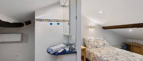 A bedroom with a bed, a bedside table, a mirror, a small bathroom with a sink and a toilet.