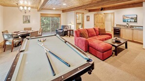 Ein gemütliches Wohnzimmer mit Billardtisch, einem roten Sofa und einem Essbereich mit Stühlen.