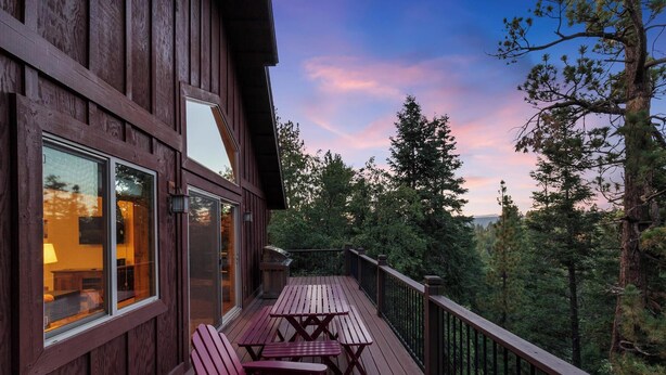 Eine Holzterrasse mit roten Adirondack-Stühlen und einem Tisch, mit Blick auf ein bewaldetes Gebiet.