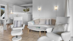 A modern, white-themed living room with a sofa, armchairs, and a coffee table. There is a kitchen area in the background with white cabinetry and a hanging light fixture. - "Rolfkarl" - 250m from the sea by Interhome (Mesinge)