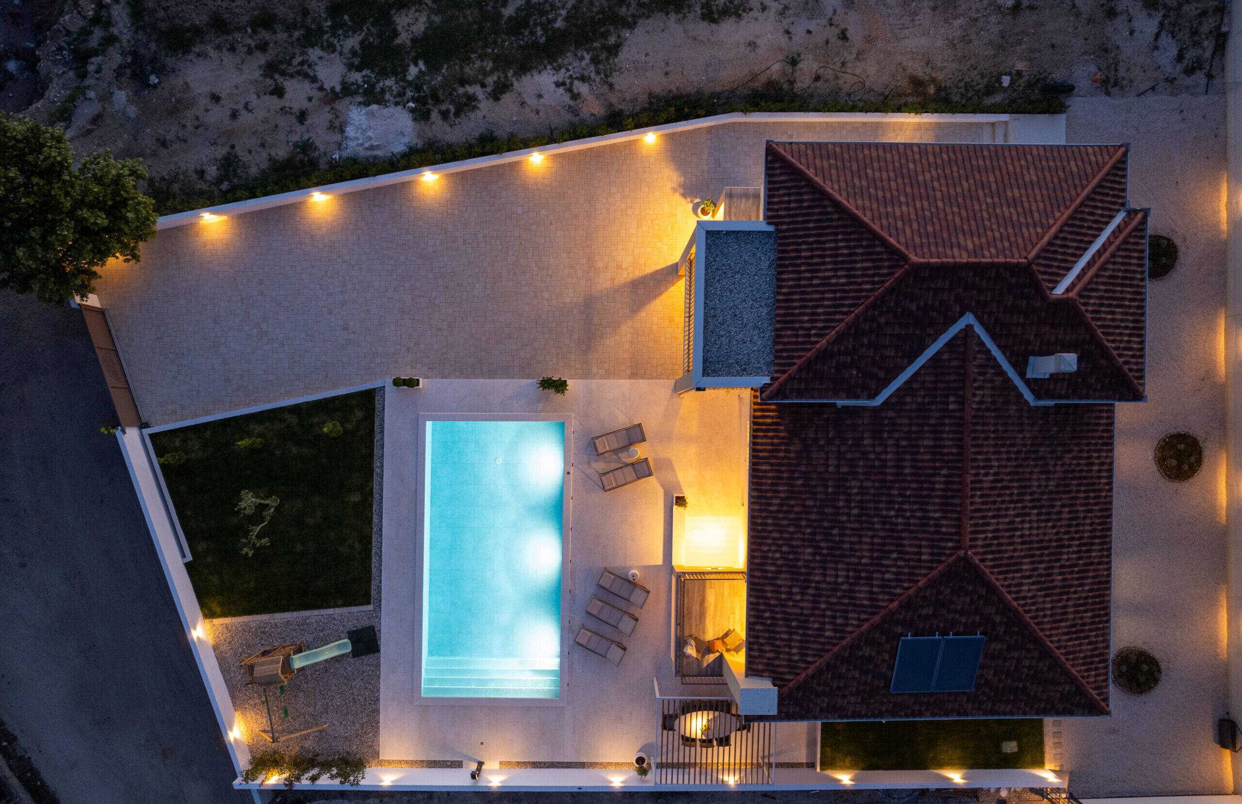 Vista aérea de una casa con piscina, mobiliario de exterior y un patio bien iluminado.