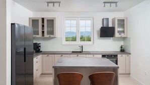 A modern kitchen with a large island, two bar stools, a built-in oven, and a window with a view.