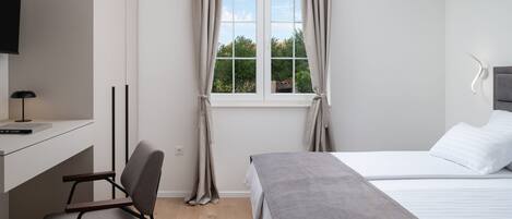 A bedroom with a bed, a desk with a chair, a TV, and a window with curtains.