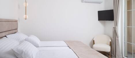 A hotel room with two beds, a flat-screen TV, an air conditioning unit, and a chair by the window.