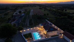 A modern house with a swimming pool, outdoor seating, and a view of the sunset over fields.