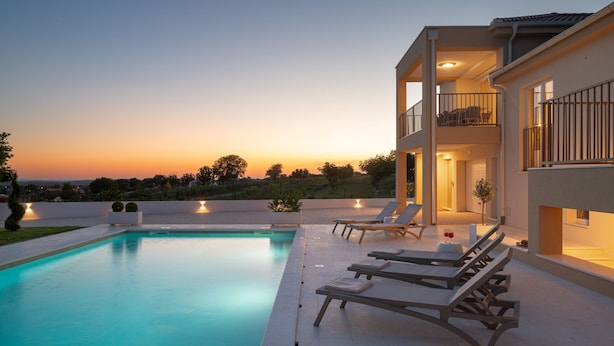 A modern two-story house with a swimming pool, outdoor seating, and a balcony with a railing.