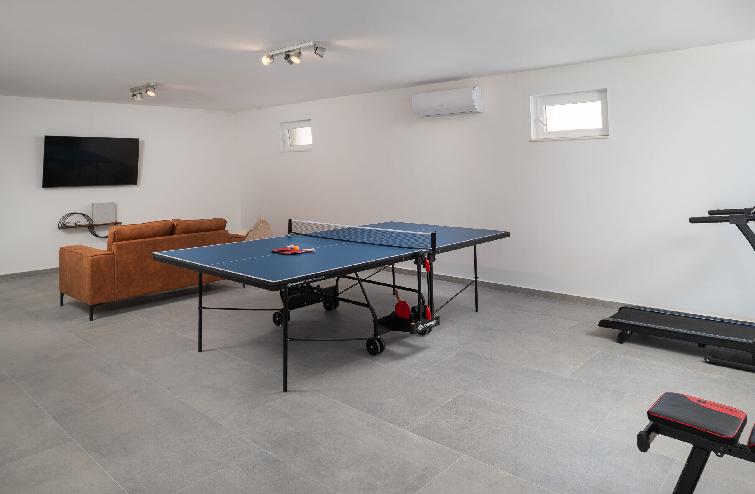 Une pièce équipée d’une table de ping-pong, d’un canapé, d’un tapis de course et d’un téléviseur.