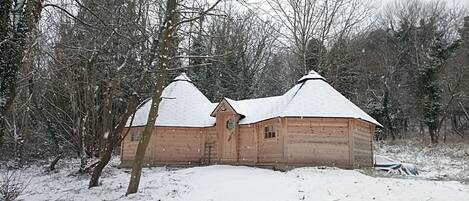 Una cabaña de madera con techo nevado, rodeada de árboles y nieve.
