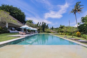 A rectangular swimming pool with a clear blue water surface, surrounded by a well-maintained lawn and various trees.