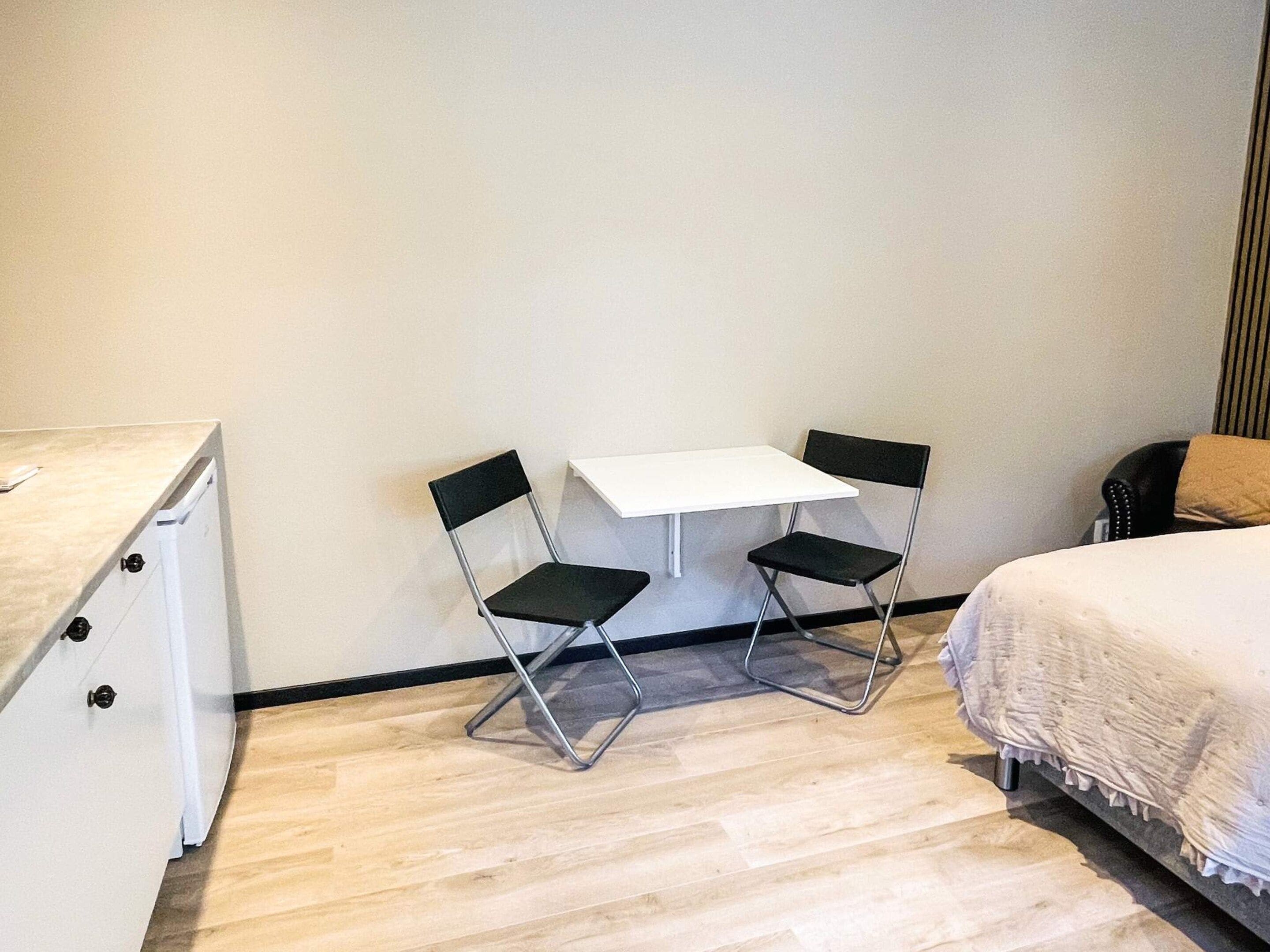 Una habitación pequeña y sencilla con cama, escritorio y dos sillas.