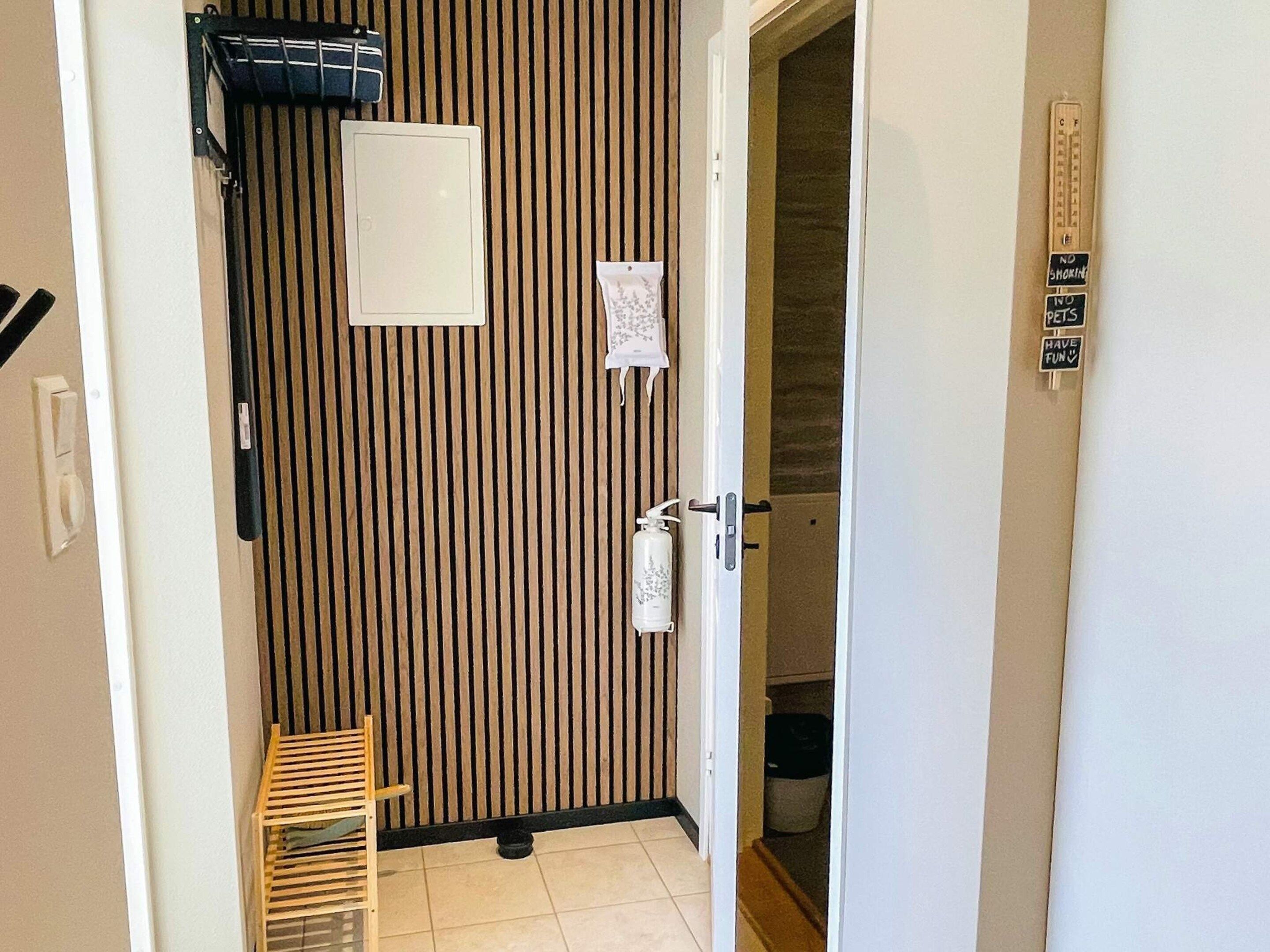 A narrow hallway with a wooden slat wall, a door with a towel hanging on it, and a small wooden bench.