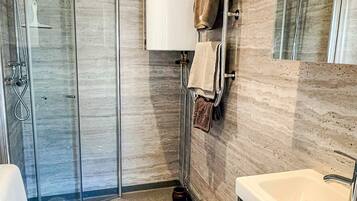 A modern bathroom with a glass shower enclosure, a white sink, and a towel rack with towels.