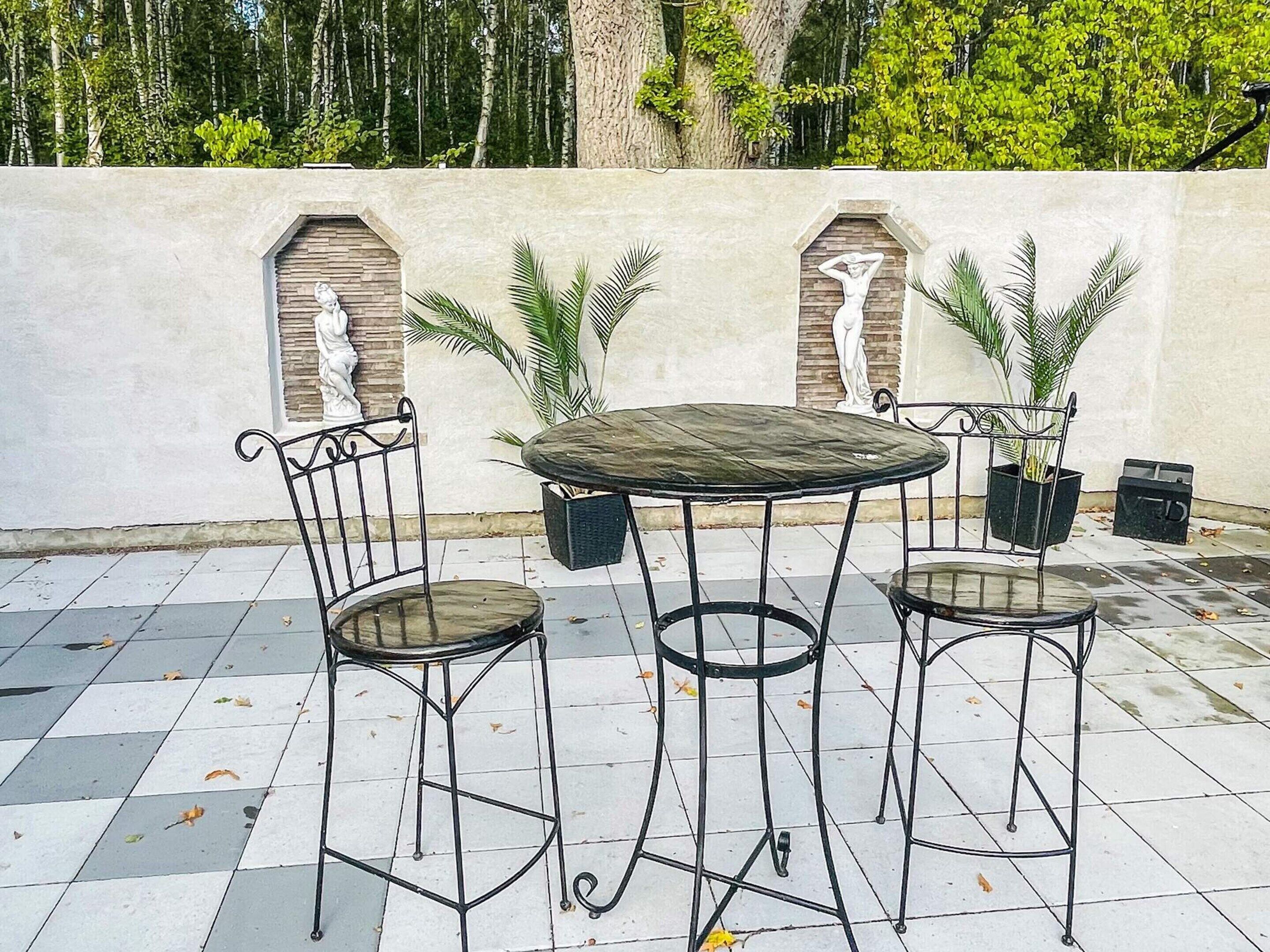 A patio with a round table and two chairs, surrounded by potted plants and decorative wall niches.