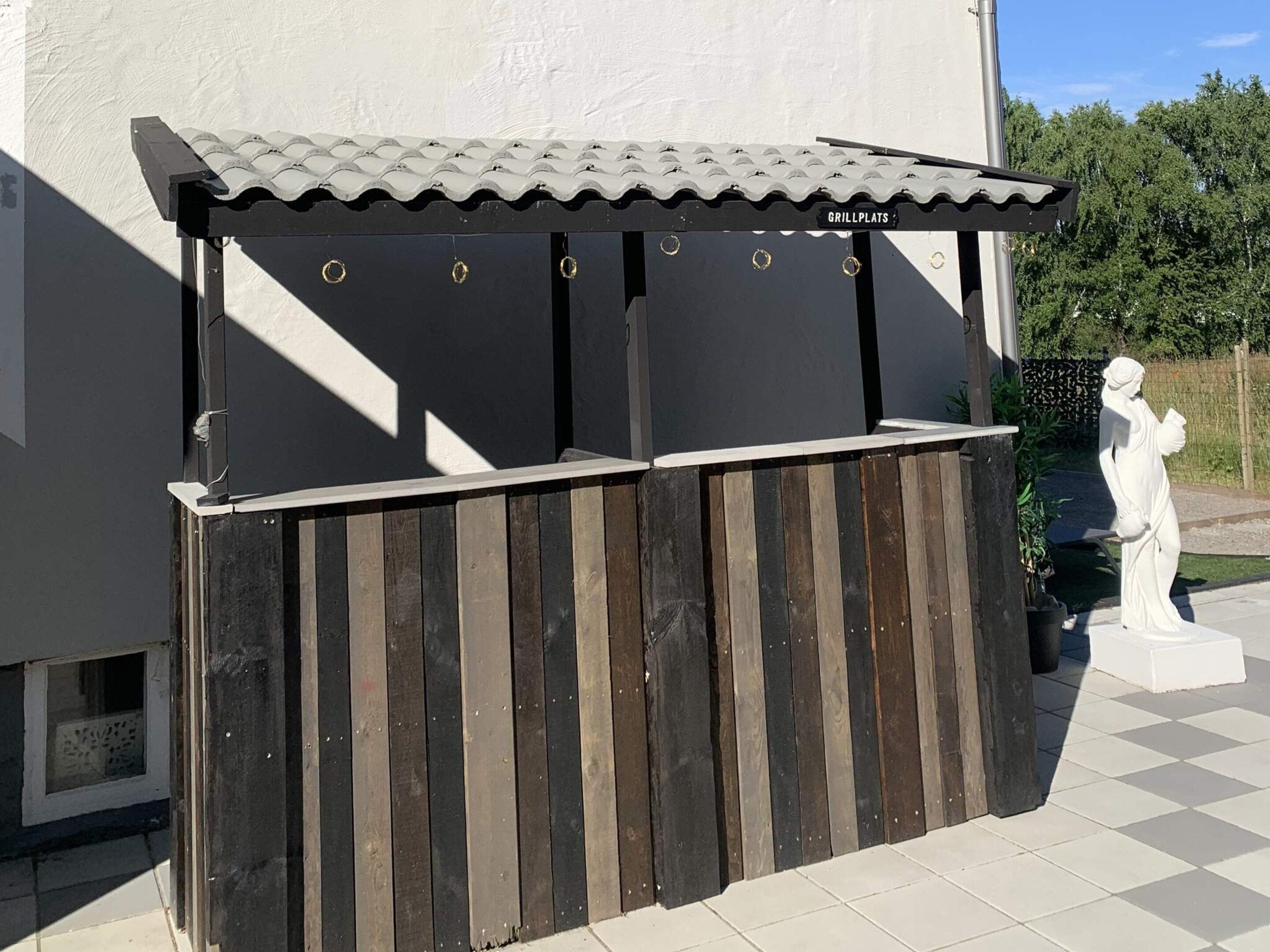 A grill area with a tiled roof and a wooden fence.