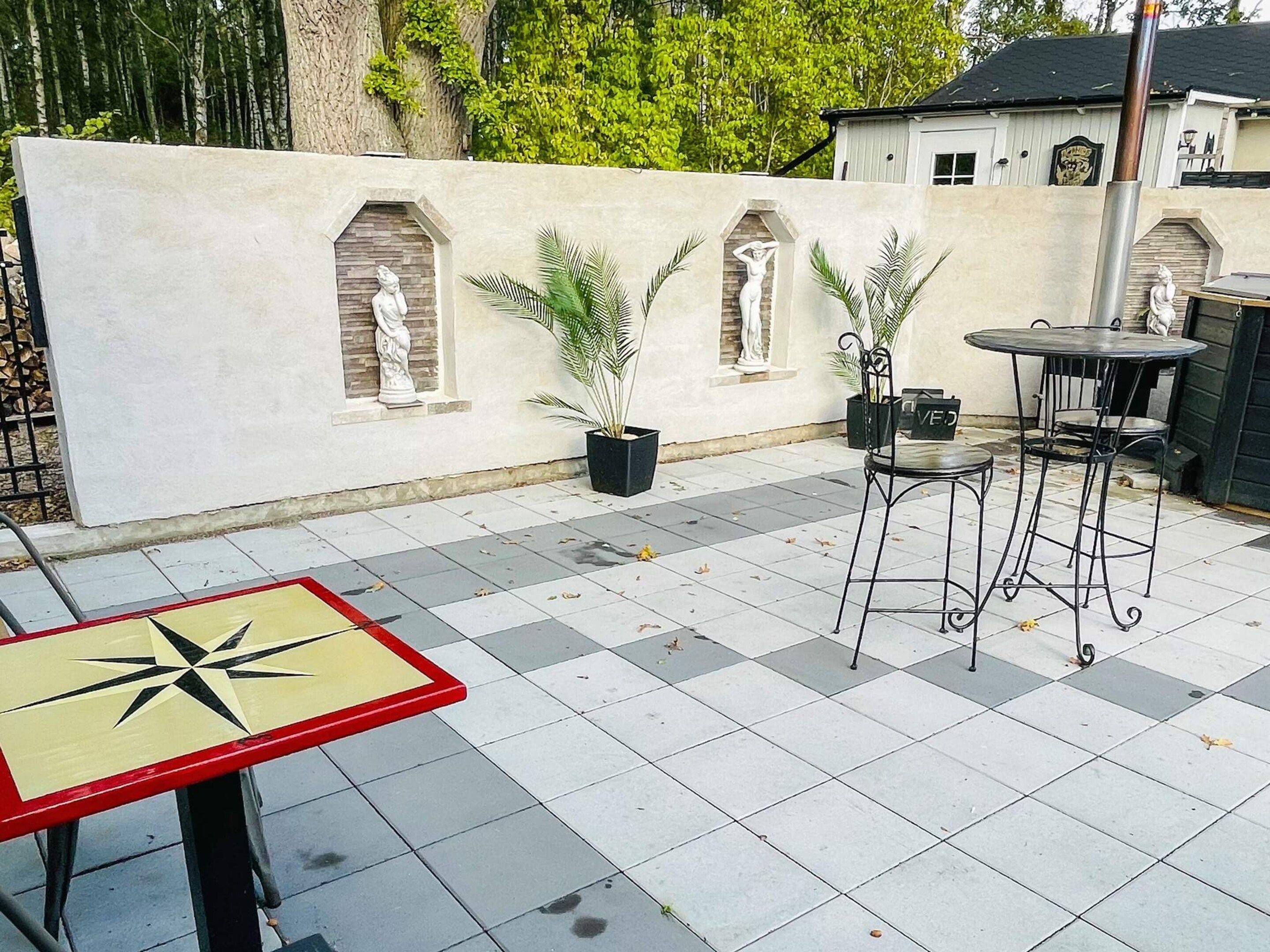 Una zona patio con pavimento piastrellato, tavolo in metallo e sedie, e nicchie decorative con statue.
