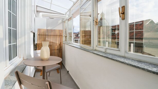 Ein sonnendurchfluteter Raum mit Tisch und Stühlen, ein großes Fenster mit Blick auf Gebäude und ein Holzzaun.