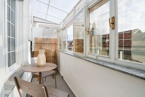 A sunlit room with a table and chairs, a large window with a view of buildings, and a wooden fence. - Agostino Center Apartment (Turin)