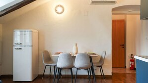 Eine kleine Küche mit einem weißen Kühlschrank, zwei grauen Stühlen, einem Holztisch und einer Wand-Klimaanlage.