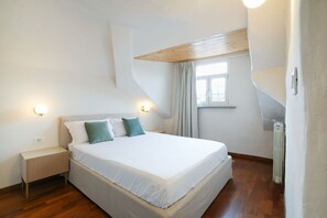 A bedroom with a bed, bedside lamps, a window with curtains, a radiator, and a sloped ceiling. - Agostino Center Apartment (Turin)