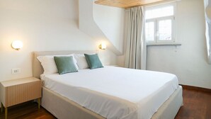 Ein Schlafzimmer mit Bett, Nachttischen, einem Fenster und einer geneigten Decke.