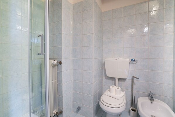 A bathroom with a glass shower enclosure, a toilet, and a bidet.