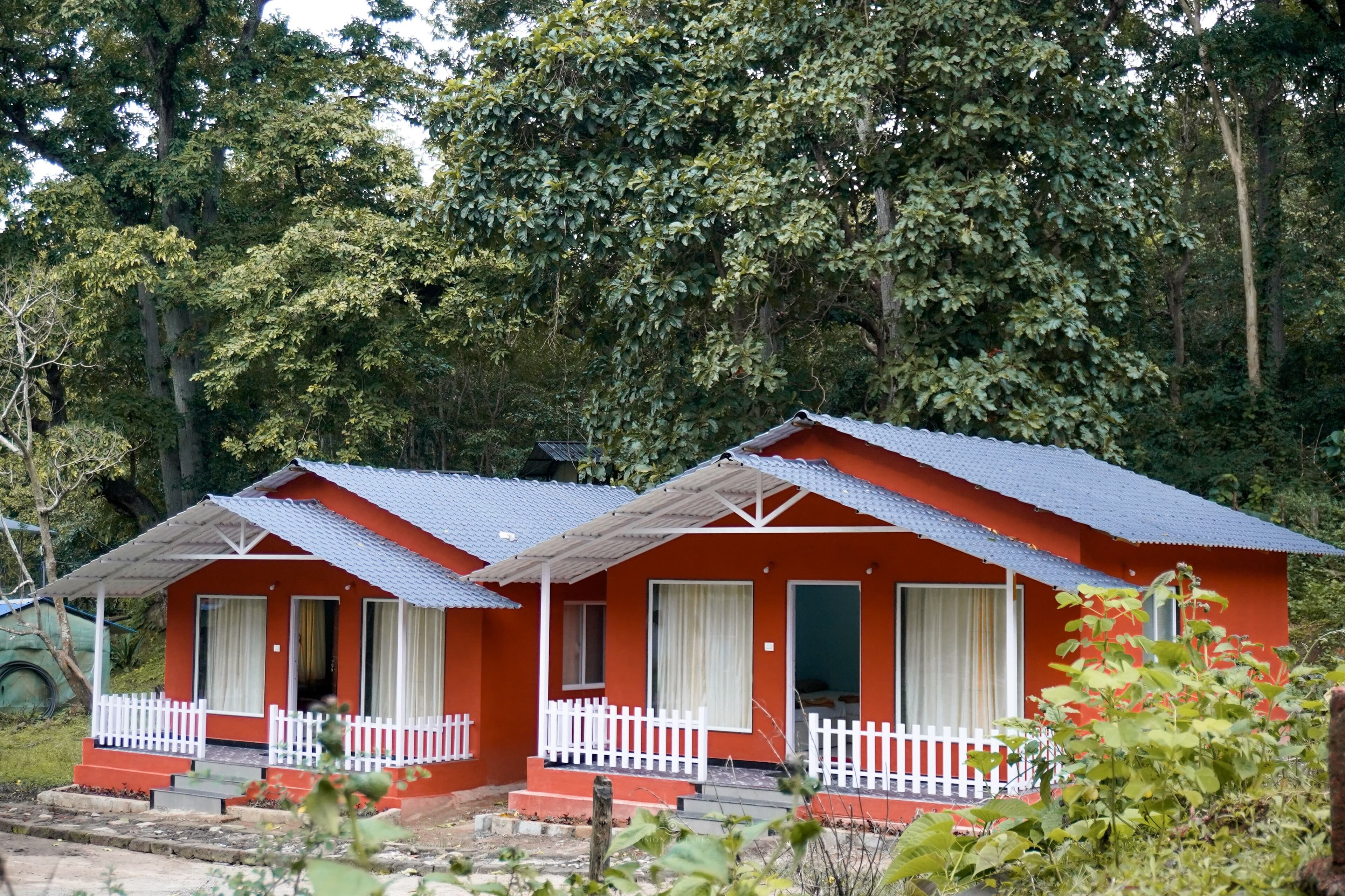 Dos cabañas rojas con barandillas blancas y techo metálico, rodeadas de un denso bosque.