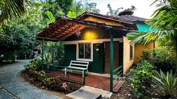 A small, single-story building with a tiled roof and a green door, surrounded by lush greenery and a stone pathway.