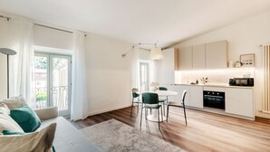 Une cuisine moderne avec des meubles blancs, une table à manger avec des chaises et une grande fenêtre avec des rideaux.
