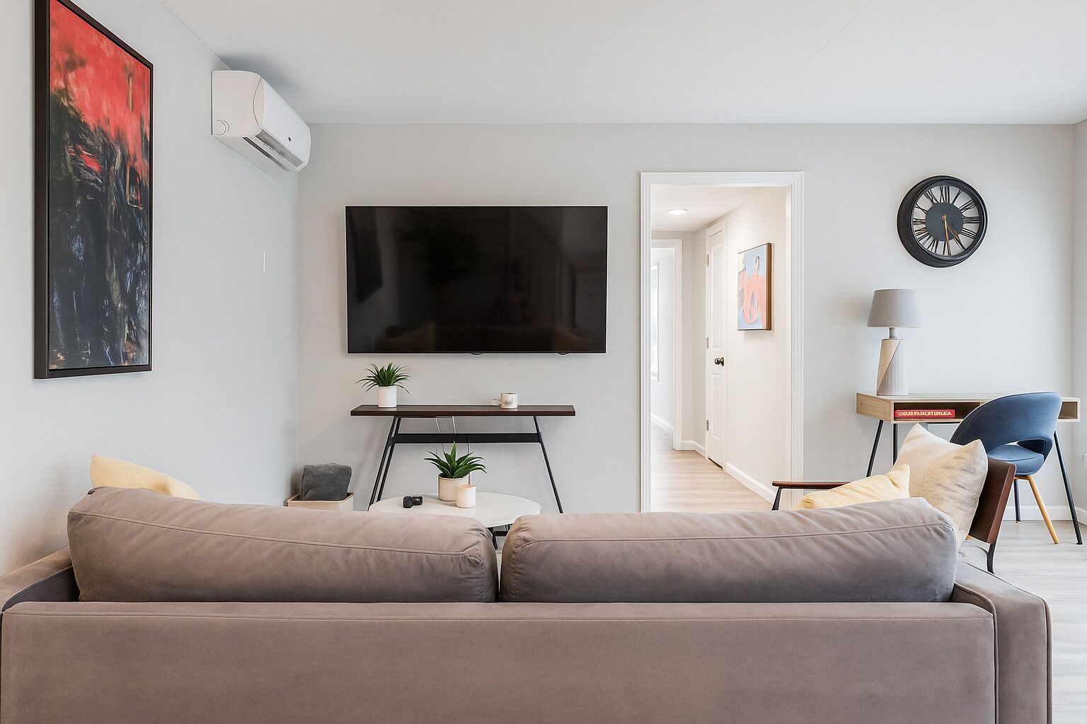 A modern living room with a large flat-screen TV, a sofa, a coffee table with plants, and a side table.