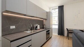 A modern kitchen with a marble countertop, integrated appliances, and a dining area with a grey sofa and table. - Milano Centro | Fontana House  (Milano)