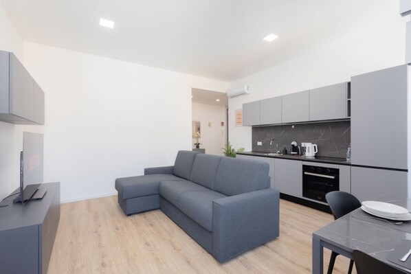 A modern kitchen with grey cabinets, a grey sofa, and a dining area with a table and chairs.