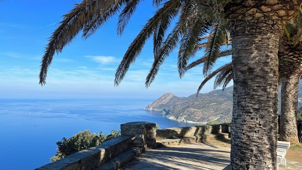 A stone pathway leading to a scenic overlook with a view of the sea and mountains.