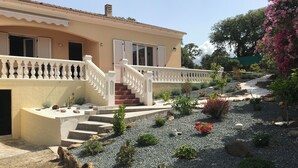 A house with a beige exterior, a white staircase, and a garden with various plants and rocks.