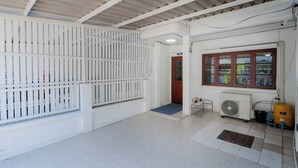 A spacious room with a tiled floor, a white partition, a window with a red frame, an air conditioning unit, and a yellow water heater. - Charming 2-bedroom House in Hua Hin Soi 80,12-minute Walk to Beach (Hua Hin)