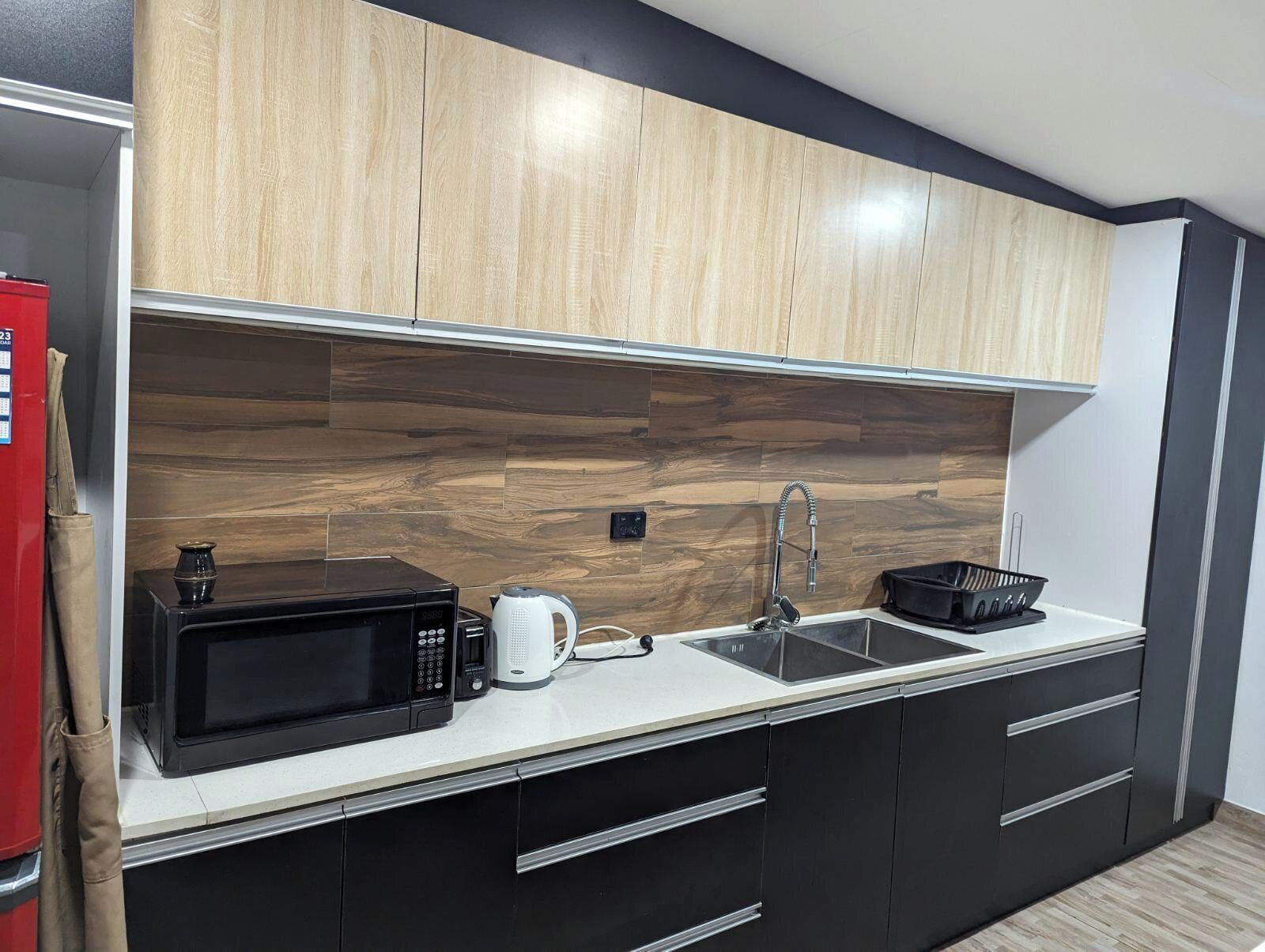 Une cuisine moderne avec des meubles en bois, un micro-ondes noir, une bouilloire et un évier.