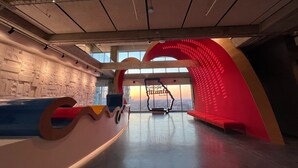 Un espacio interior amplio con un gran ventanal, una pared curva roja y una escalera.