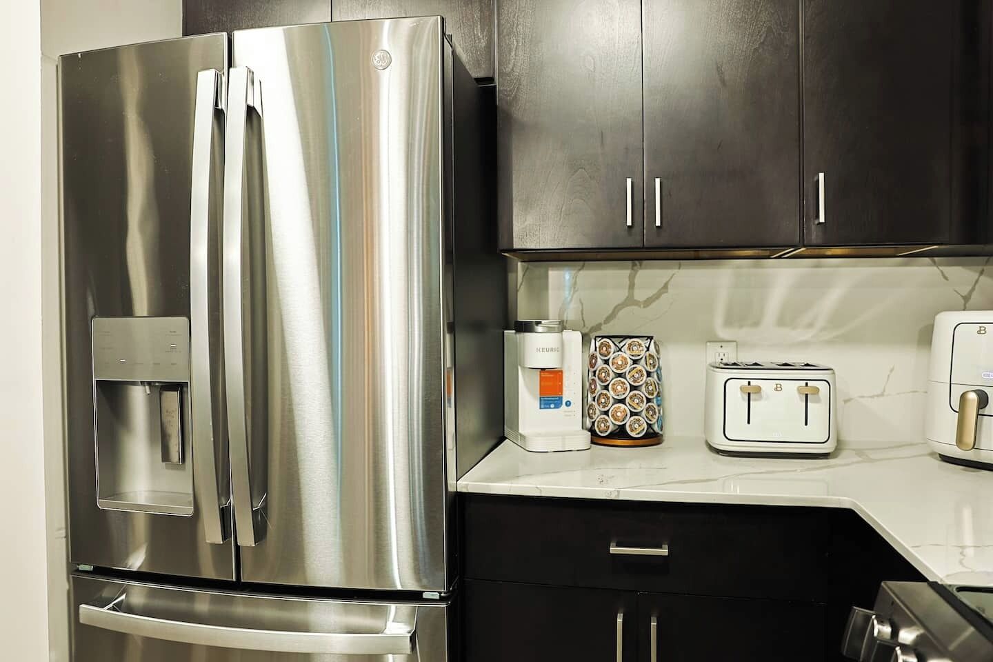 Un refrigerador de acero inoxidable, un dispensador de agua, una cafetera, un tostador y un microondas sobre una encimera de cocina.