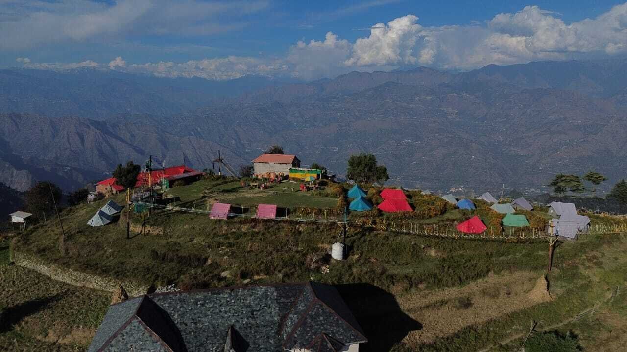 A mountainous village with several houses and a small building, surrounded by steep hills and a clear sky.