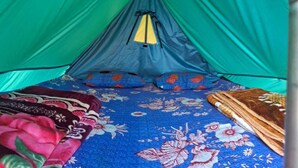 A tent with a blue and floral interior, a sleeping bag, and a yellow tent peg. - DhaulaPir Adventure (Chamba)