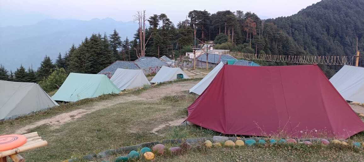 A campsite with multiple tents, a dirt path, and a mountainous backdrop.