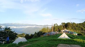 A mountainous area with several tents and buildings, likely a campsite or lodge. - DhaulaPir Adventure (Chamba)