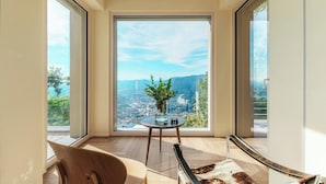 Ein modernes Zimmer mit großen Fenstern und Blick auf die Stadt, ein runder Tisch mit Pflanzenvase und ein Ledersofa.