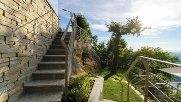 A stone staircase with metal railings leading to a grassy area with a view of the sea.