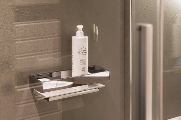 A bathroom with a white bottle of 'My Home' organic soap on a chrome shelf.